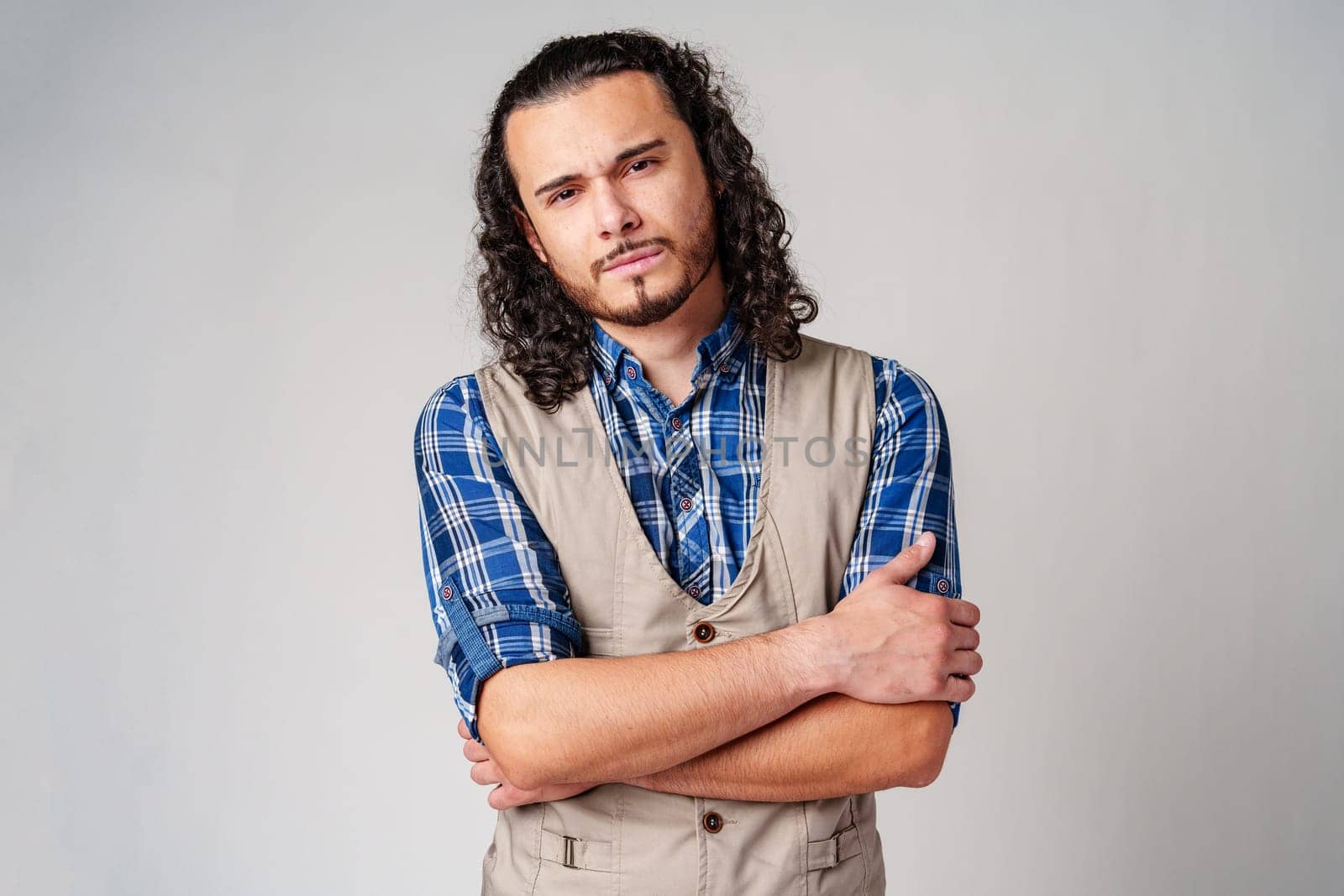A confident young man with curly hair poses against a neutral backdrop indoors