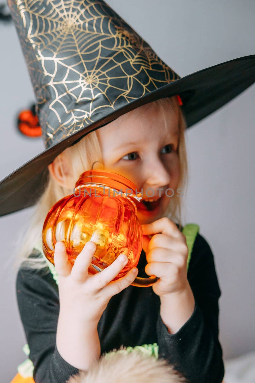 Children's Halloween - a girl in a witch hat and a carnival costume with airy orange and black balloons at home. Ready to celebrate Halloween.