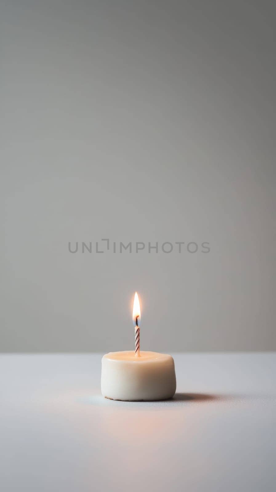 A small birthday cake with a single candle on plain background.