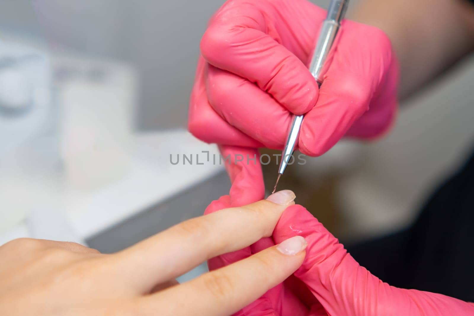 Manicurist in pink gloves uses a small brush to smooth out a layer of base gel polish at beauty salon