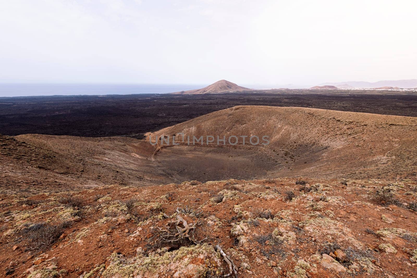 picturesque view of crater of volcano against mountains under light sky in Natural Park of Lanzarote in Canary Islands, Spain, concept of volcanic landscape and wild nature