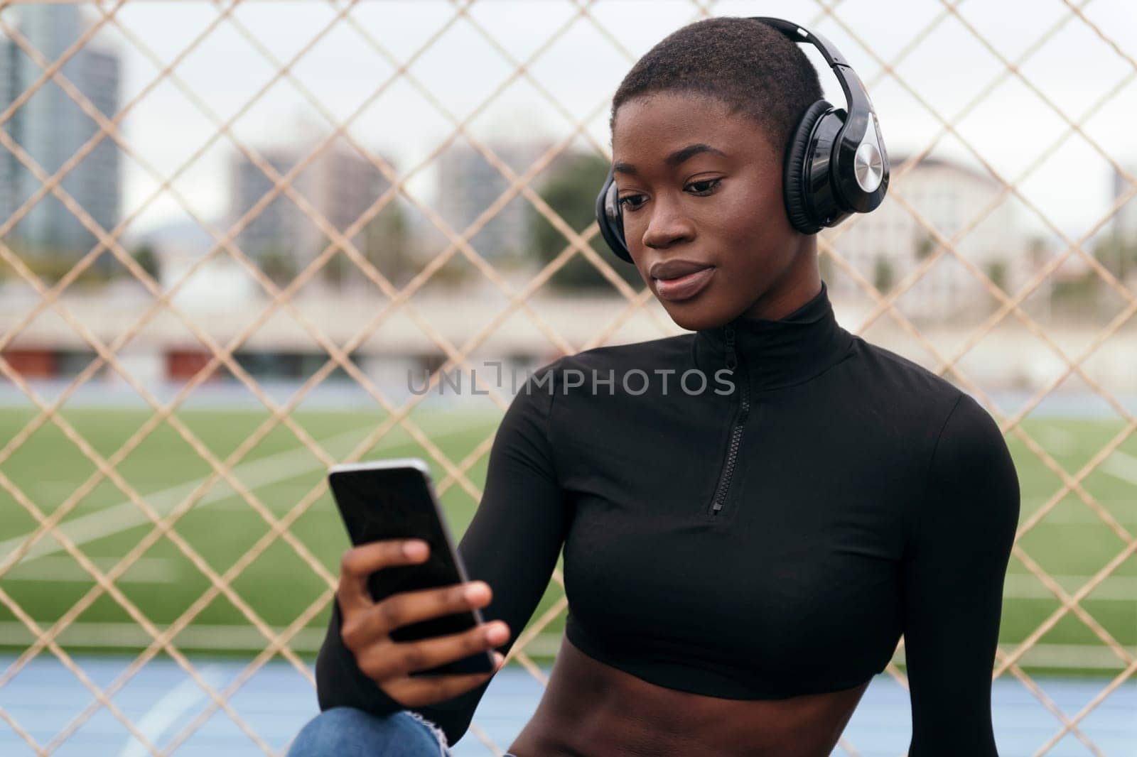 young glad ethnic female in wireless headphones surfing internet on cellphone while listening to song in city