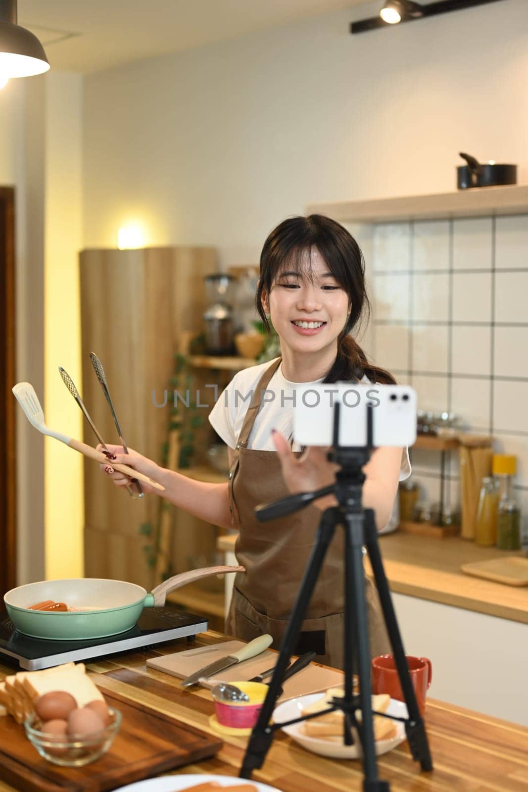 Attractive woman blogger cooking and recording video with her mobile phone in the kitchen.