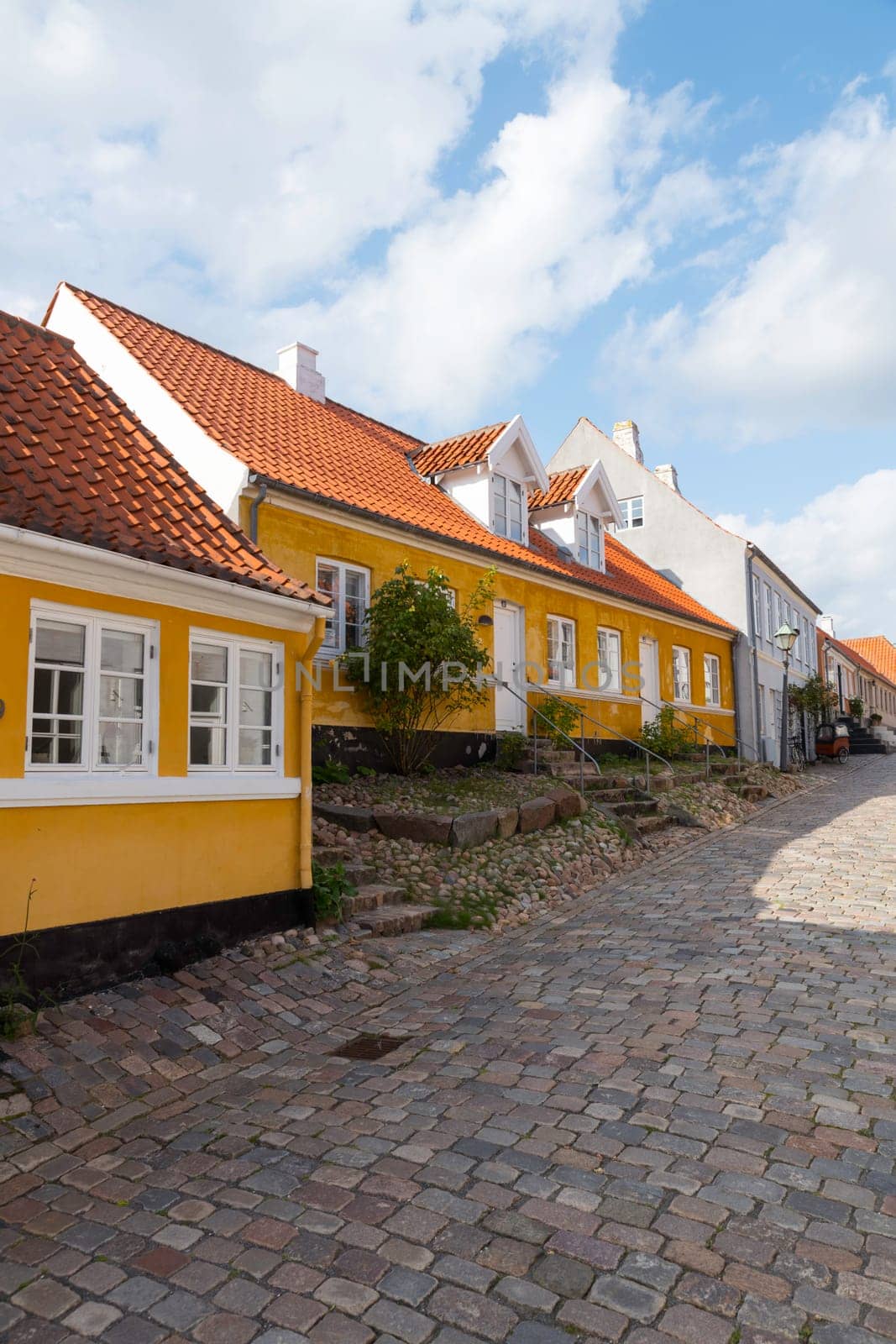ebeltoft,denmark,30-08-2024:Quaint European street featuring vibrant buildings and cobblestone path under a blue sky. typical yellow houses