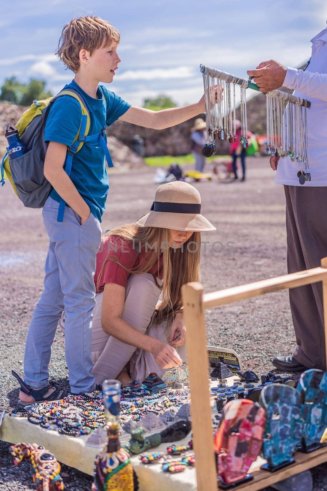 Mother and son tourists buying Mexican souvenirs from a street vendor at the foot of the Teotihuacan pyramid. Cultural experience, travel, and local craftsmanship concept.