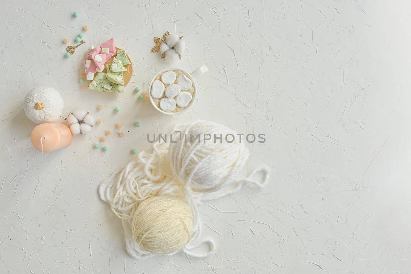 A delicate arrangement of yarn balls, pastel colored beads, and crafting materials on a light textured surface.