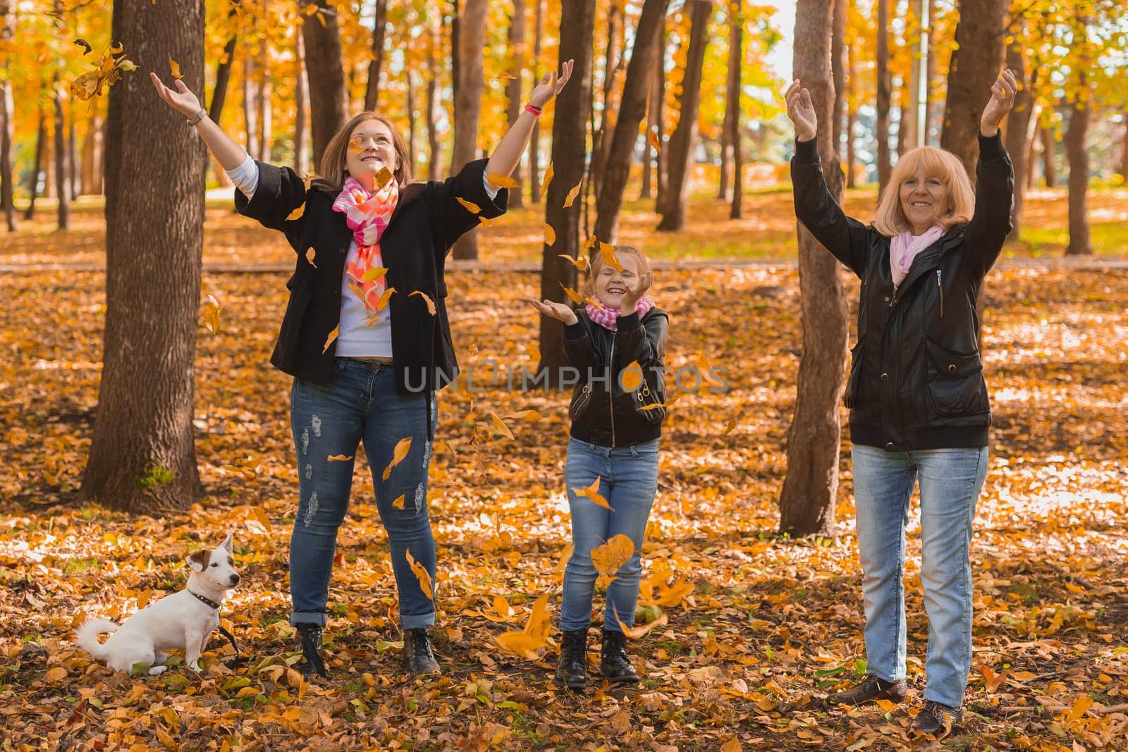 Grandmother and mother with granddaughter throw up fall leaves in autumn park and having fun. Generation, leisure and family concept. by Satura86