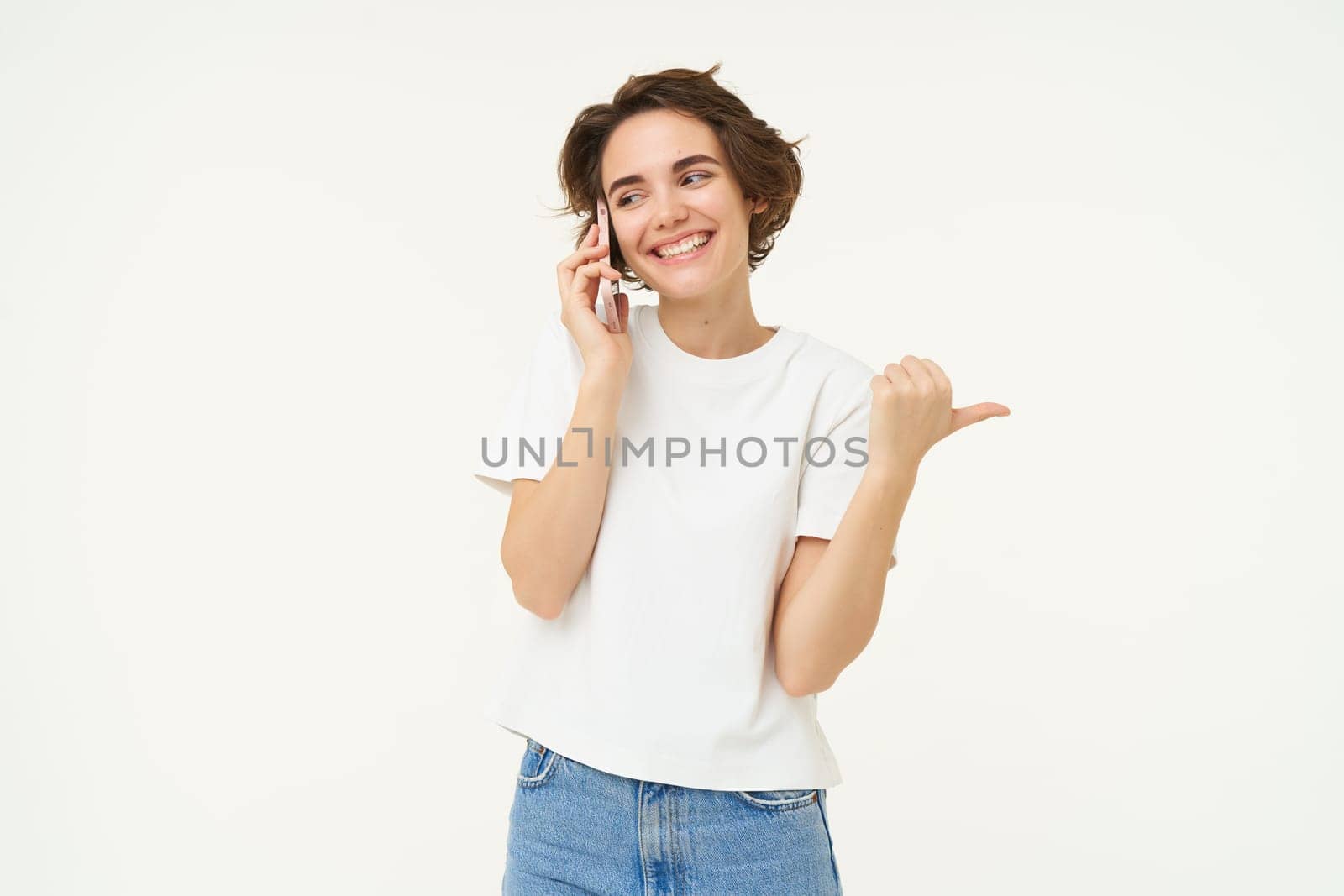 Portrait of young woman talking on mobile phone, using smartphone and pointing finger right, showing direction, banner advertisement, studio background by Benzoix