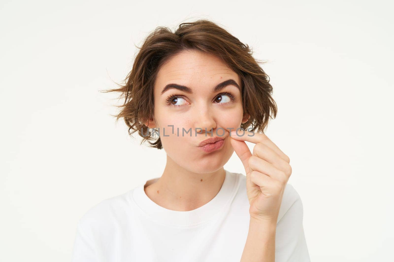 Image of young woman makes promise to keep secret, shows mouth zip gesture, puts a seal on her lips, dont talk sign, stands over white background.