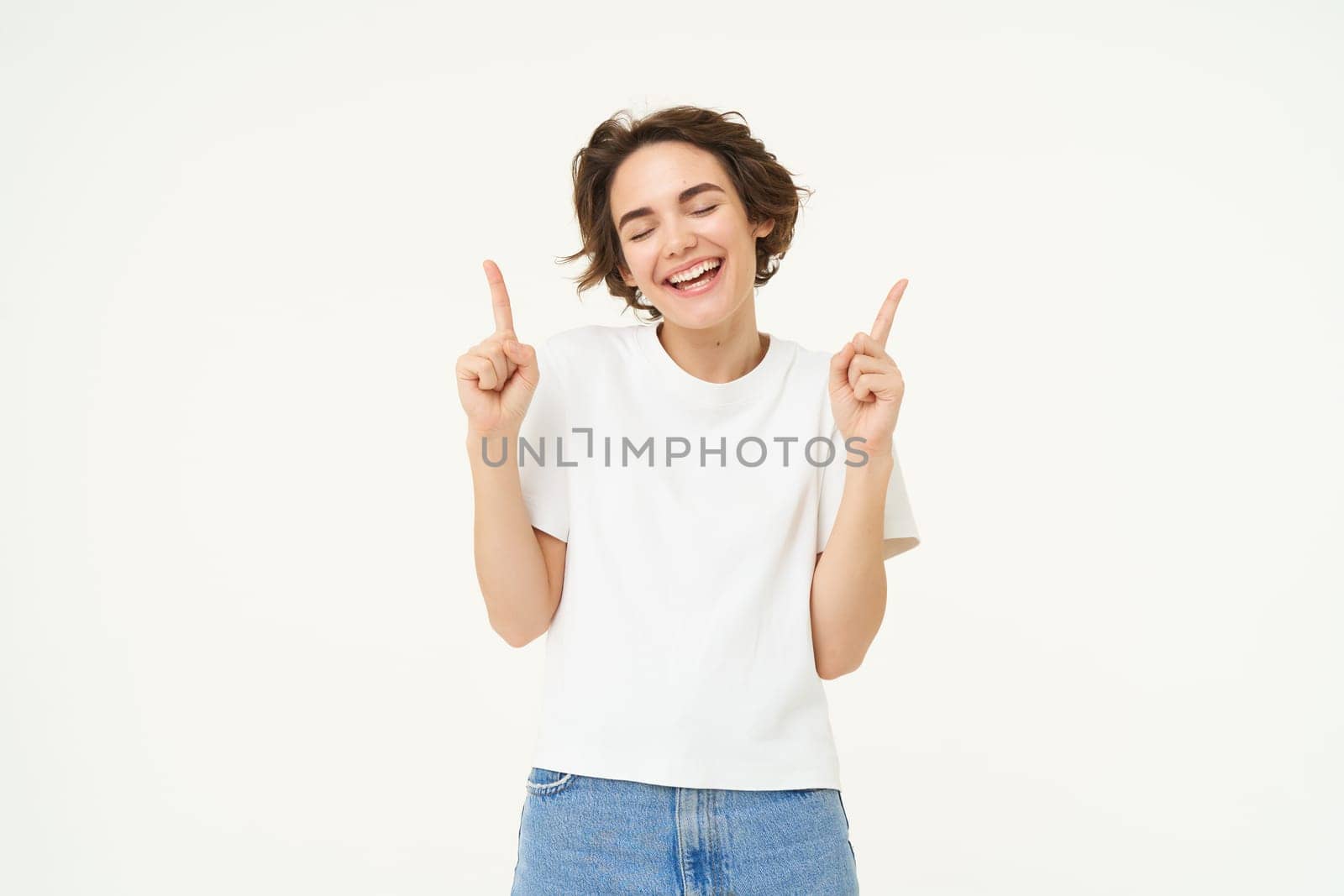 Image of carefree girl, laughing and smiling, pointing fingers up, showing promo offer, banner on top, posing over white studio background. Copy space