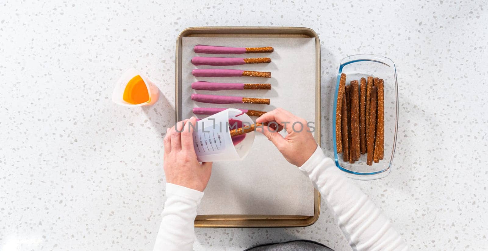 Flat lay. Dipping pretzel rods into melted chocolate to make Halloween chocolate-covered pretzel rods.