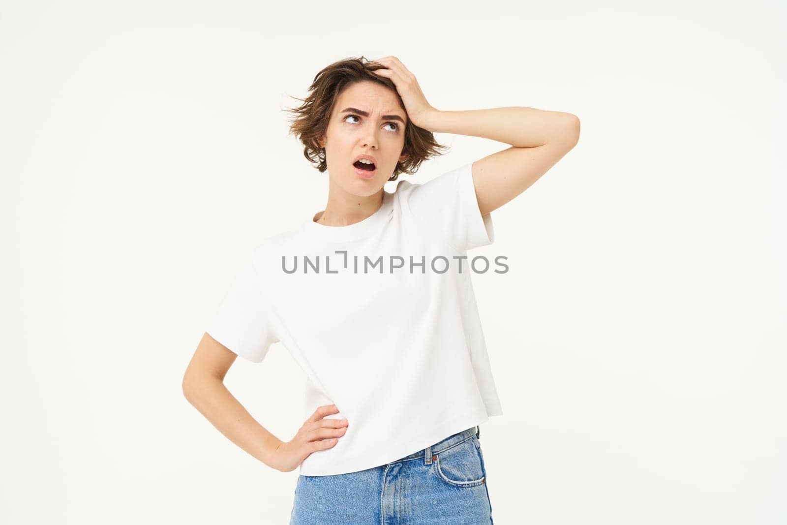 Portrait of complicated woman, touches her head, looking up, puzzled by something, feeling distressed, has problem, stands over white background.