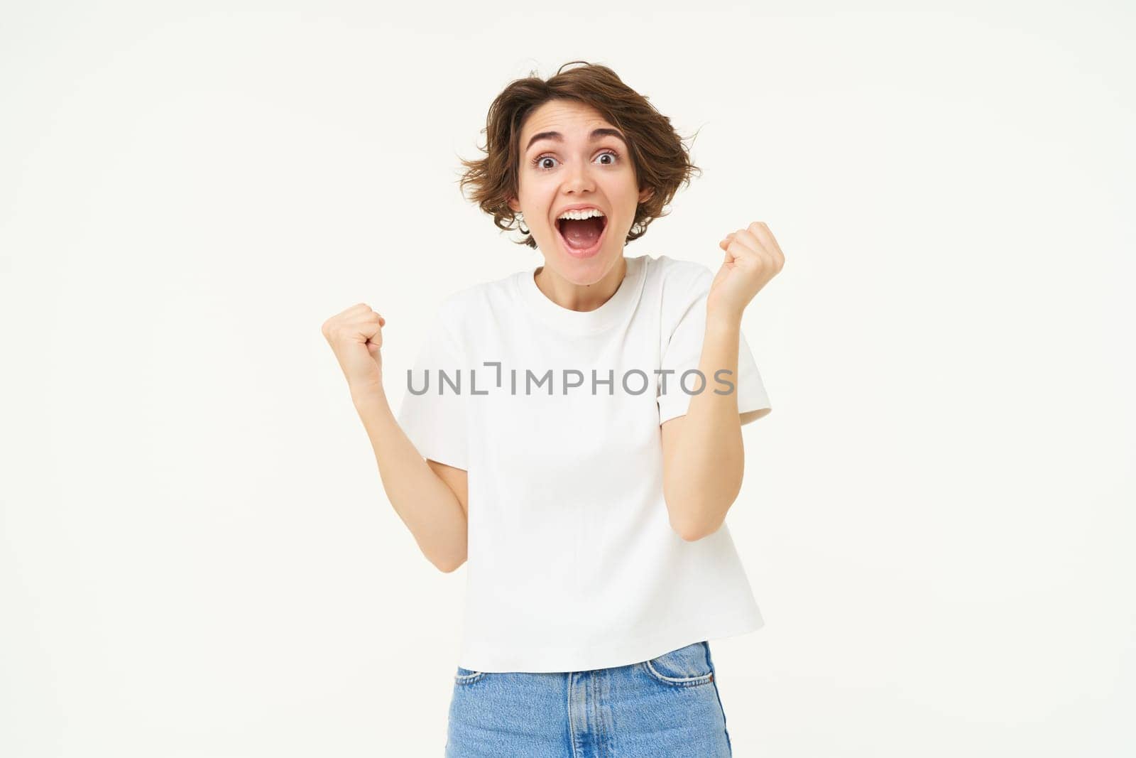 Excited brunette girl, student winning prize, celebrating victory, triumphing, standing in white t-shirt and jeans over white background by Benzoix