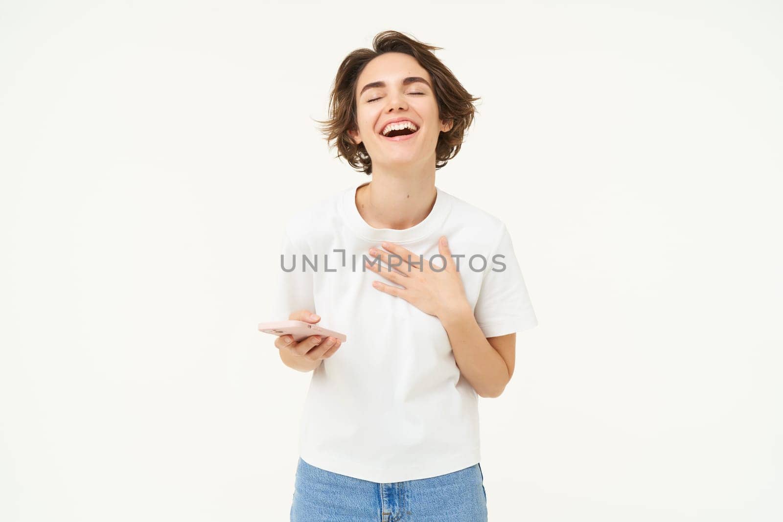 Portrait of young brunette woman texting, sending a message on telephone, using mobile phone and smiling, standing over white studio background.
