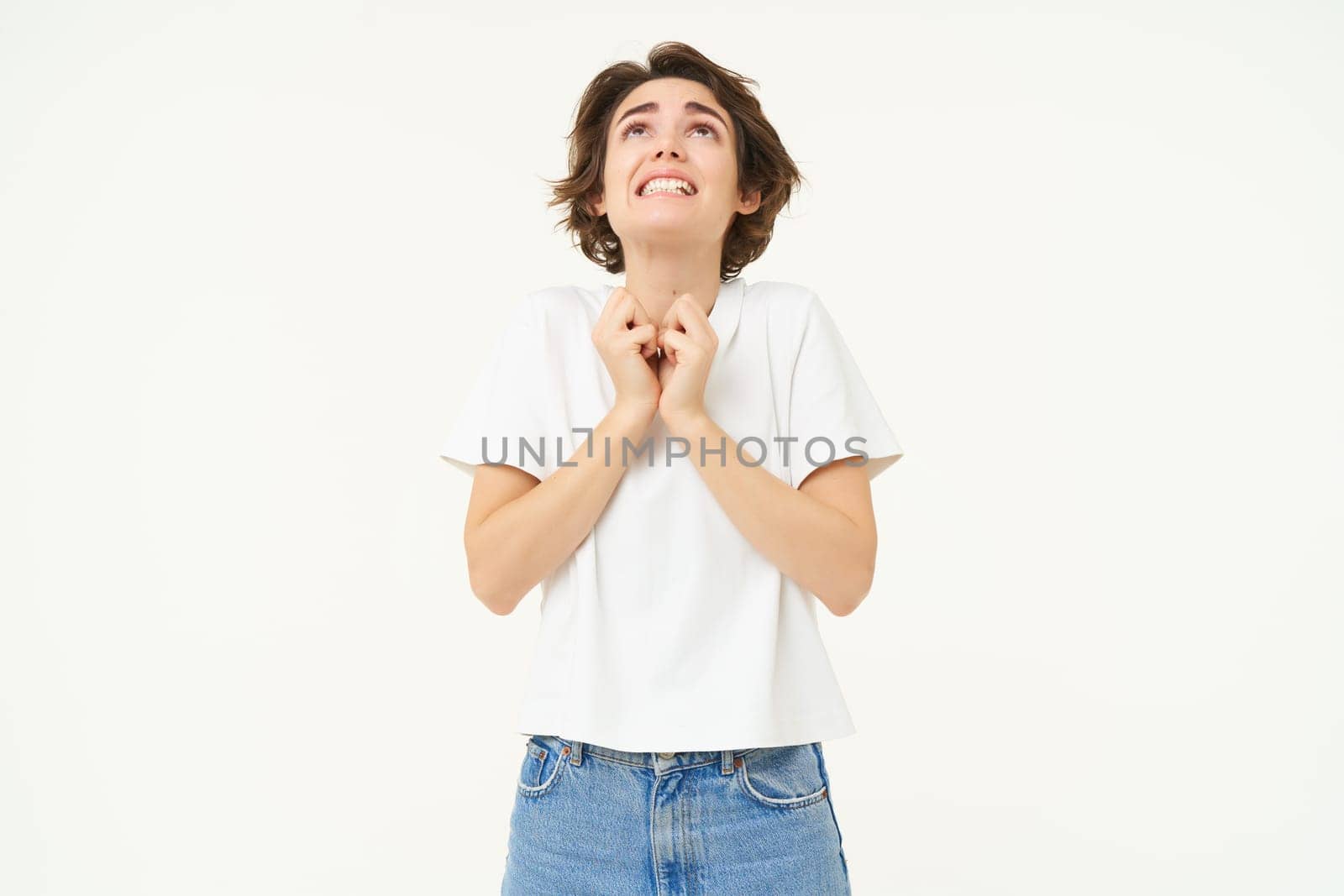 Portrait of girl looking with begging face, holding hands in pray, pleading, making wish, standing over white studio background by Benzoix