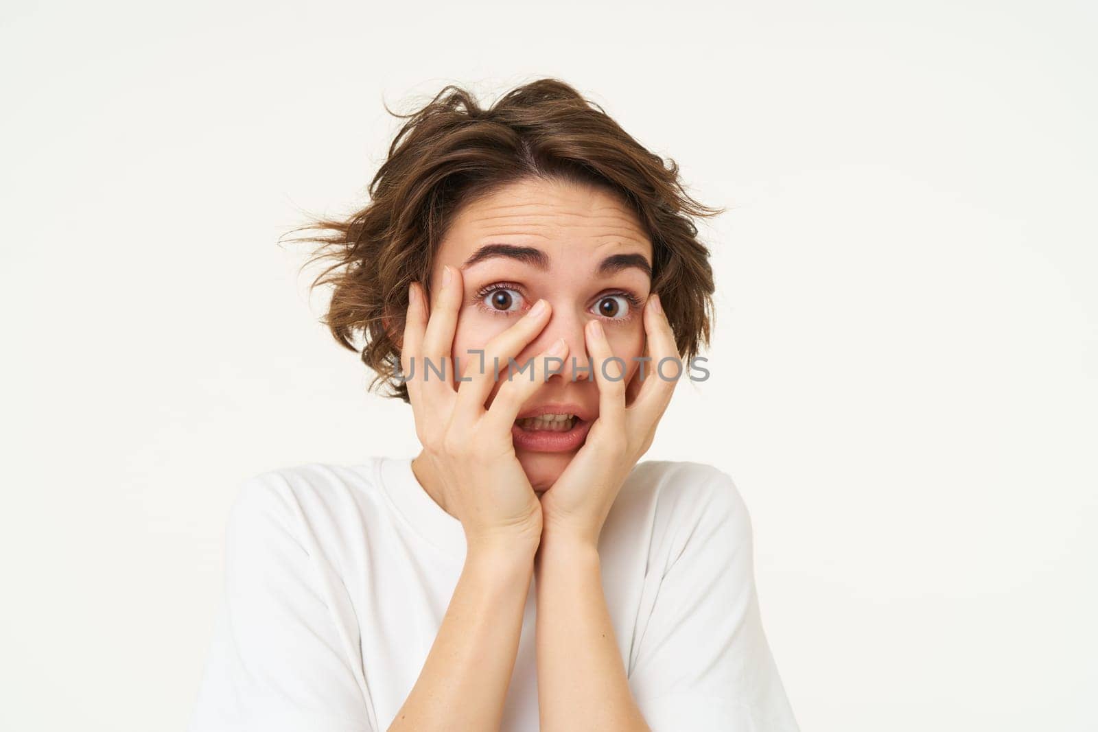 Image of girl screams and looks scared, hides face with hands, stands over white background by Benzoix