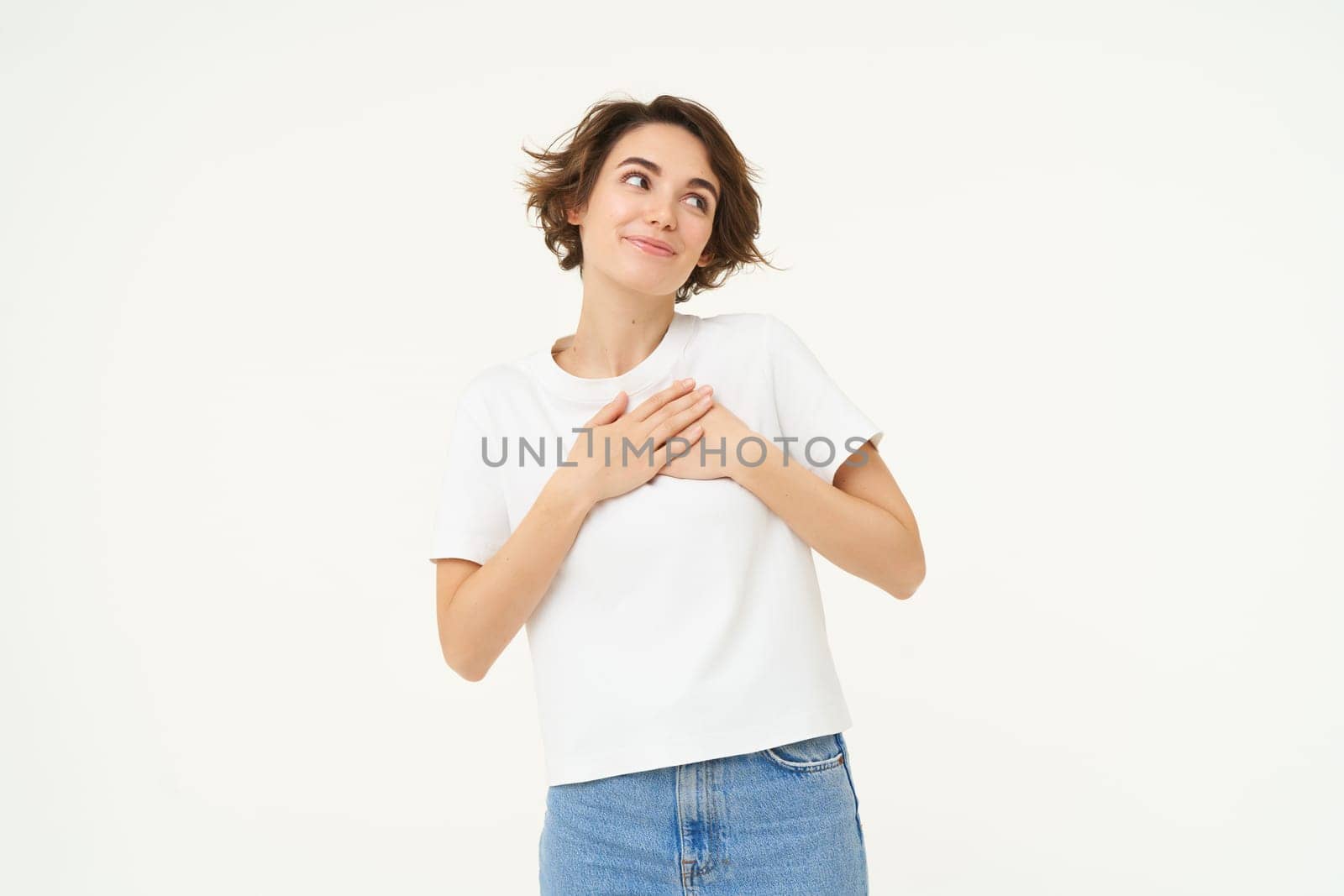 Portrait of woman expressing care, self-love and caring emotions, holds hands on chest, looking with smile at camera, isolated over white background.