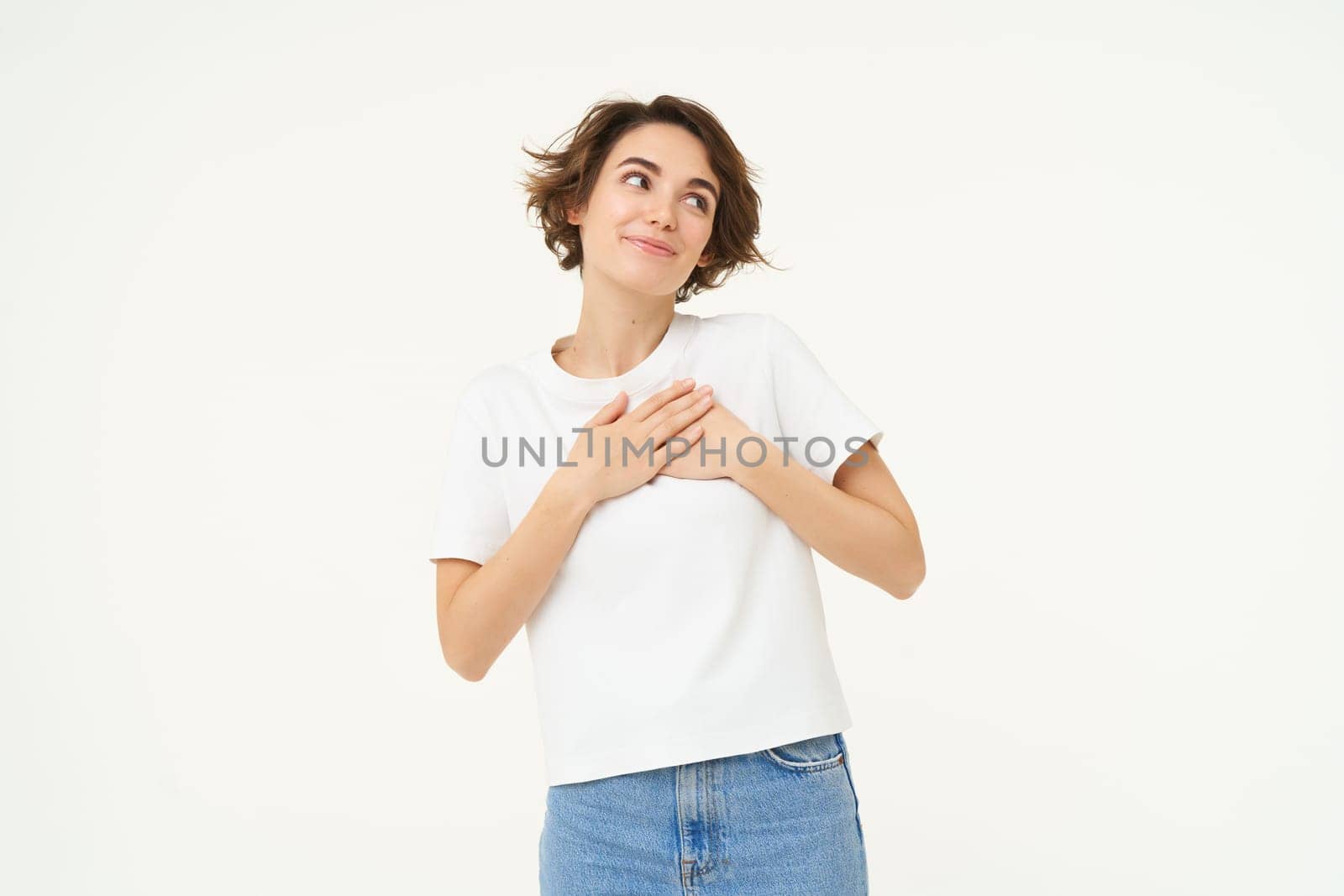 Portrait of woman expressing care, self-love and caring emotions, holds hands on chest, looking with smile at camera, isolated over white background by Benzoix