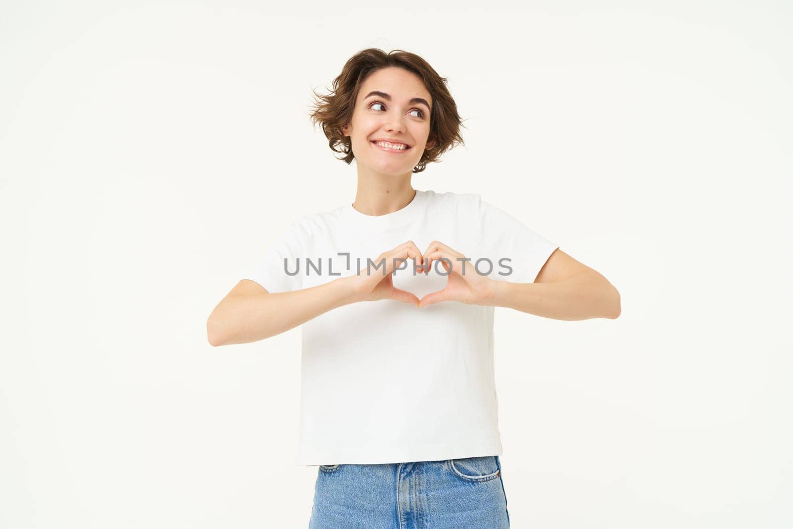 Portrait of brunette girl shows heart sign, love gesture, express care and warm feelings, stands over white background by Benzoix