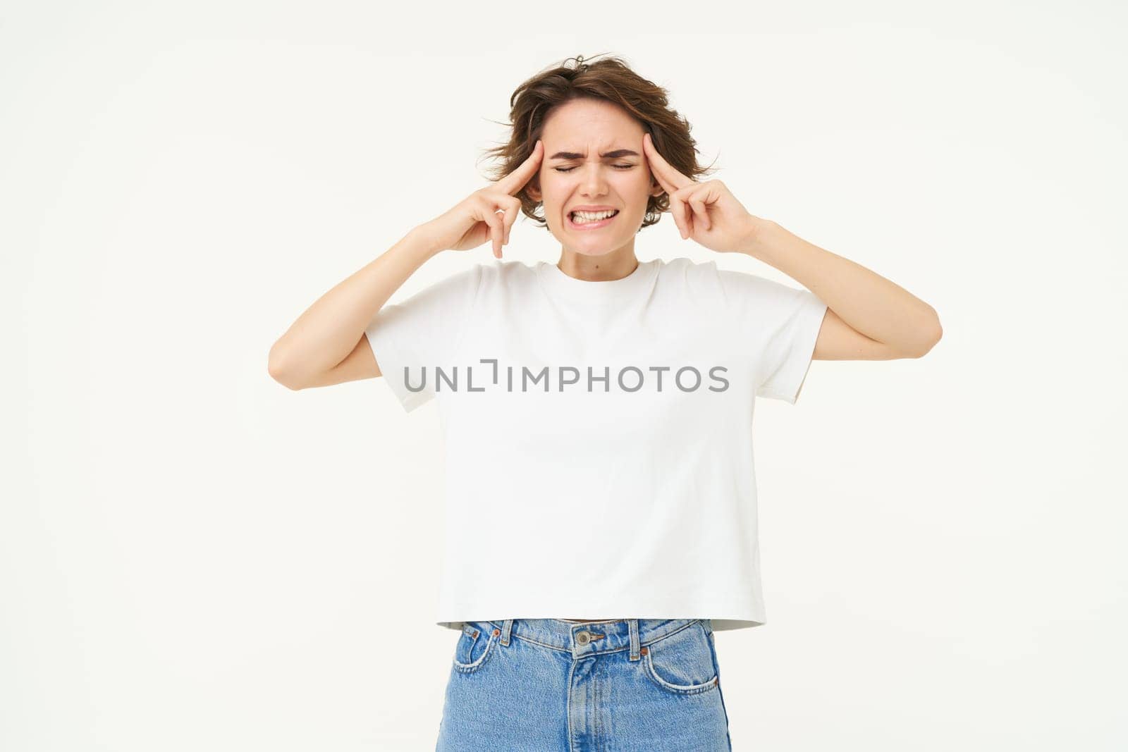 Frustrated woman, touching her head, pointing at forehead, standing with eyes clsoed and concerned face, suffers headache, thinking, trying to remember, standing over white background.