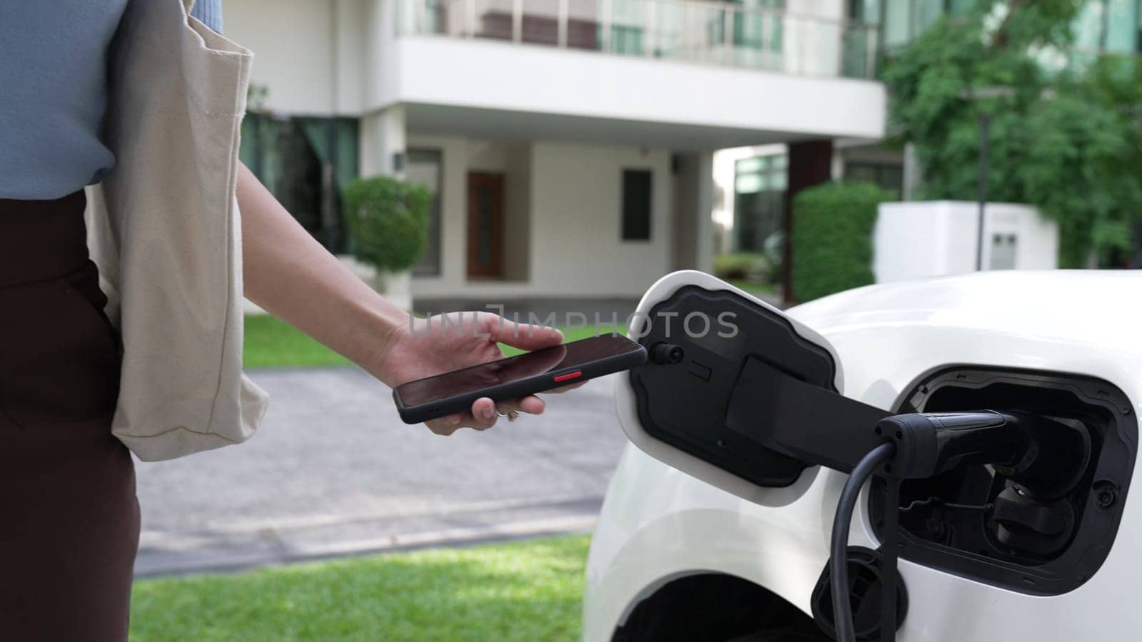 Progressive lifestyle of a modern woman who have just returned from work in an electric vehicle that is being charged at home. Electric vehicle powered by sustainable clean energy.