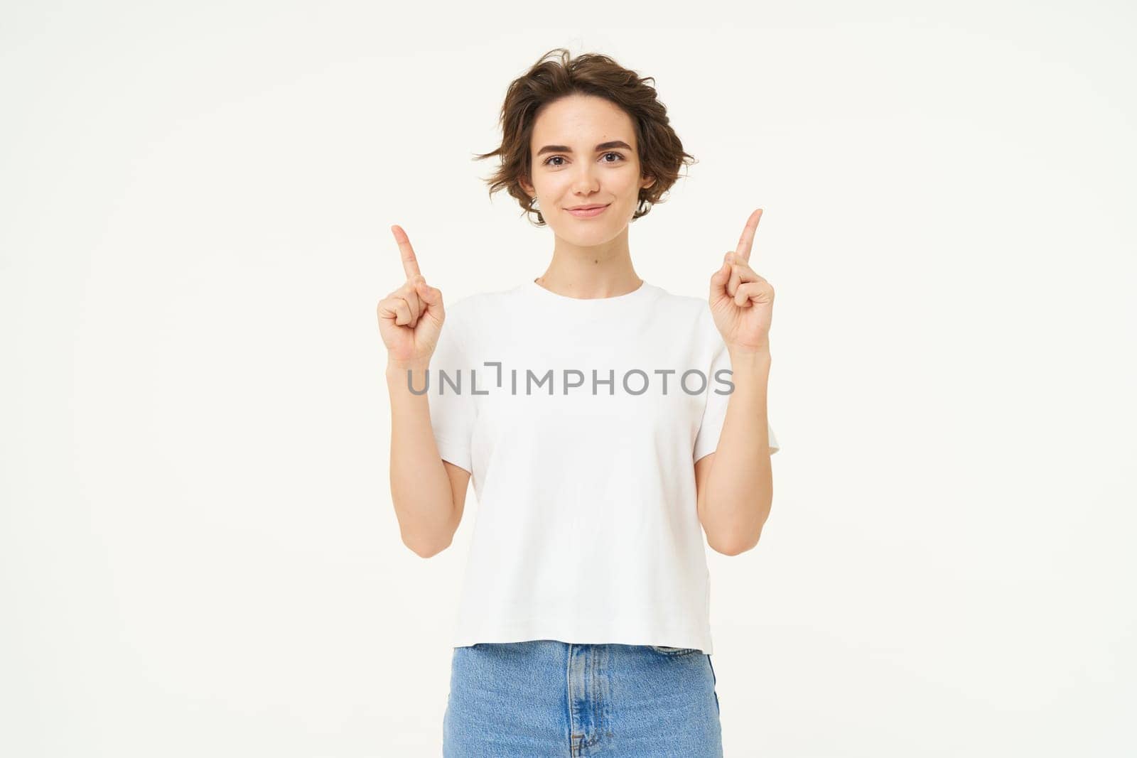 Image of happy, beautiful modern woman, pointing fingers up, showing advertisement on top, smiling, standing over white background.