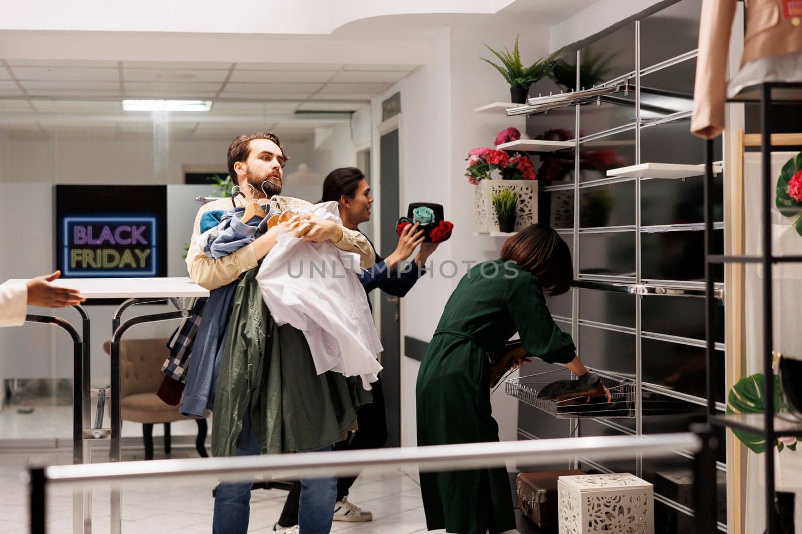 Stressed Black Friday obsessed diverse people running with clothes around fashion store with empty shelves, customers hunting for bargains during big seasonal sales in shopping mall