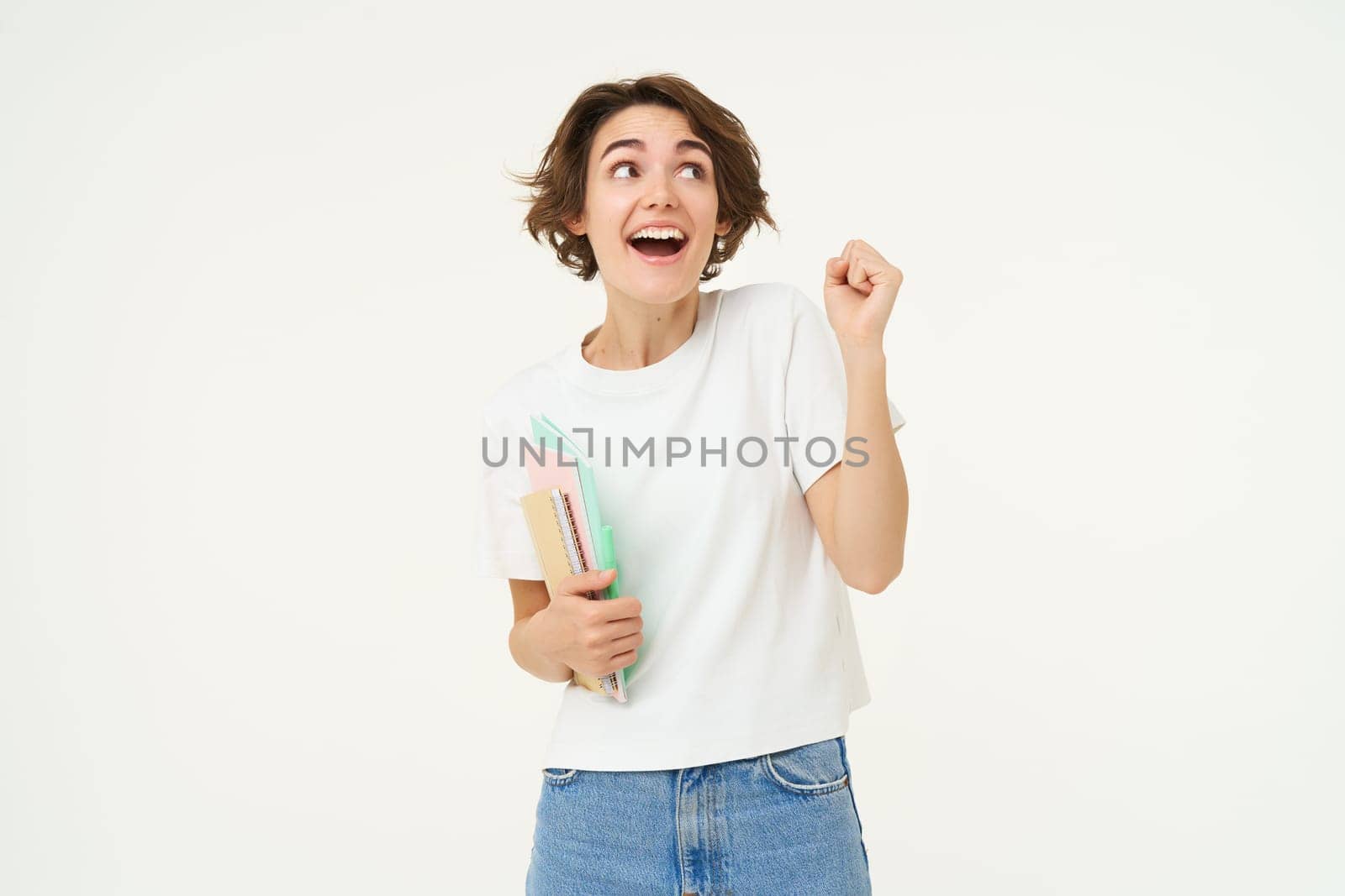 Enthusiastic brunette woman makes fist pump, holds documents and notes, looks thrilled and happy, winning, triumphing, posing over white background.