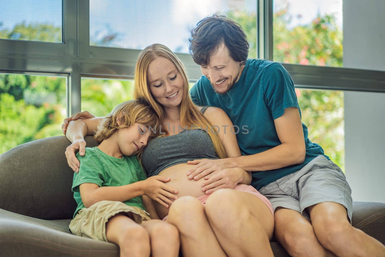 Expectant parents, mom, dad, and their eldest son share a heartwarming moment on the sofa, discussing the exciting journey of pregnancy.
