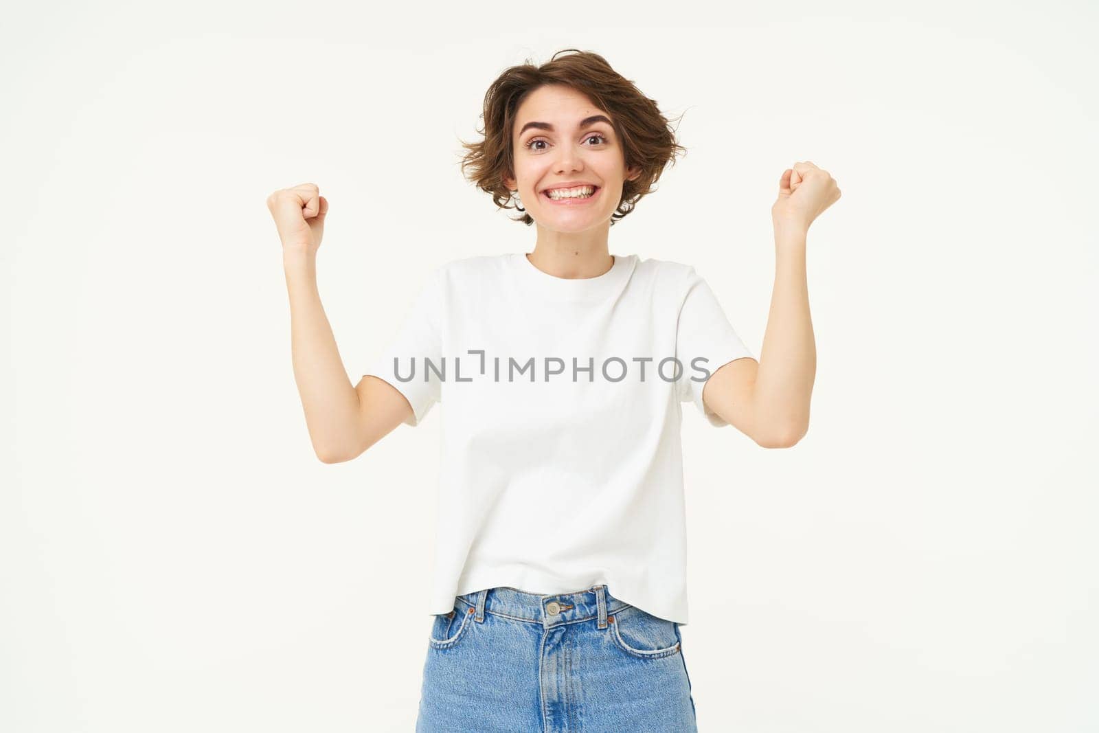 Excited brunette girl, student winning prize, celebrating victory, triumphing, standing in white t-shirt and jeans over white background by Benzoix