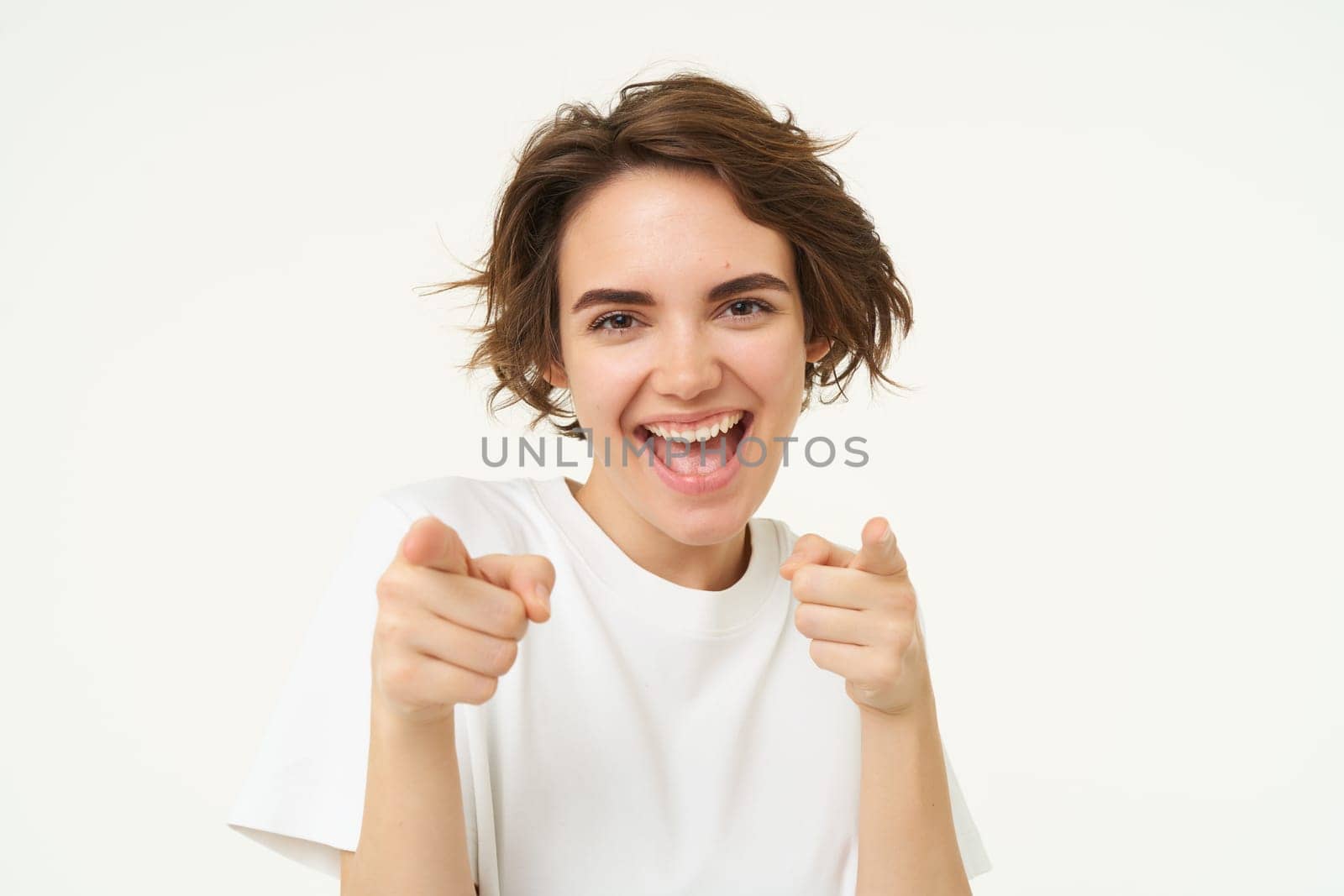 You got this. Happy modern woman, laughing and pointing fingers at you, inviting people, standing over white background.