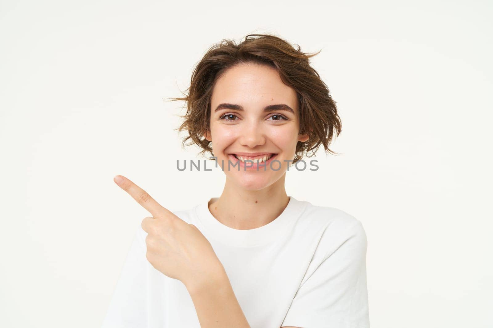 Close up shot of happy, candid woman, laughing and smiling, pointing finger left, showing advertisement, standing over white background by Benzoix