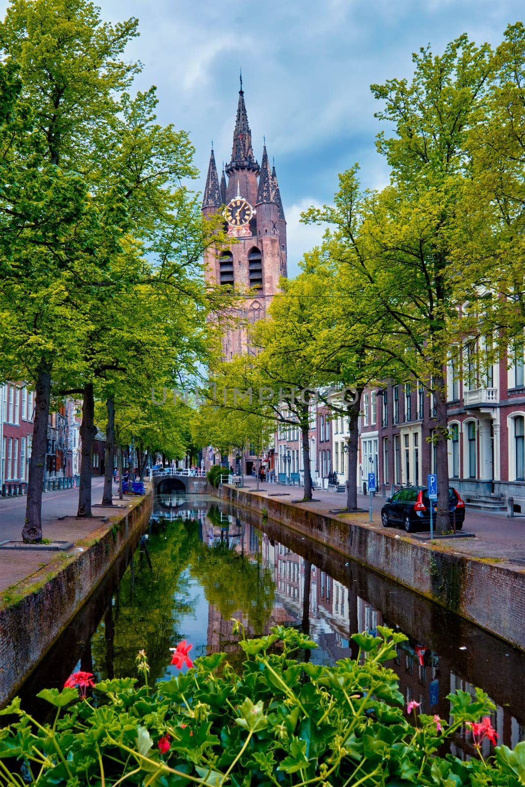 Delt canal with old houses bicycles and cars parked along and Oude Kerk Old church tower. Delft, Netherlands