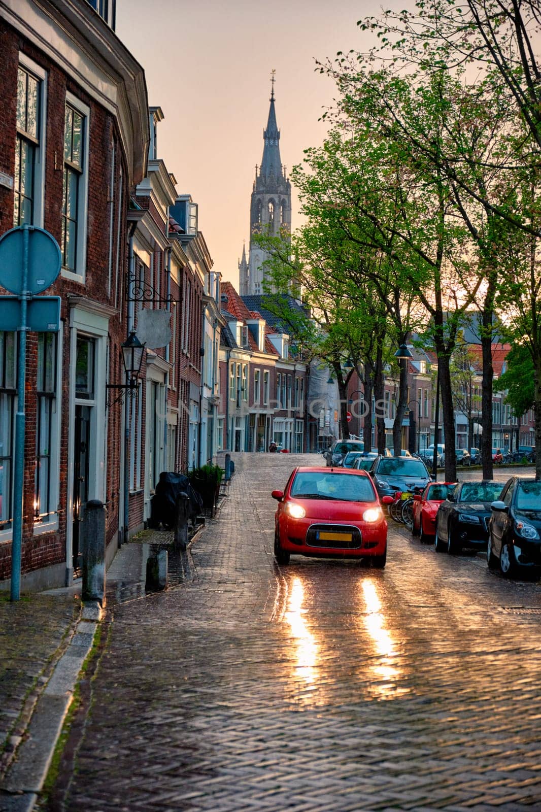 Delft cobblestone street with car in the rain with Nieuwe Kerk church tower in background. Delft, Netherlands