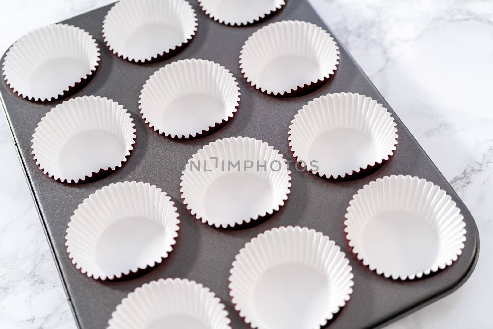 Lining cupcake pan with foil cupcake liners to bake red velvet cupcakes with white chocolate ganache frosting.