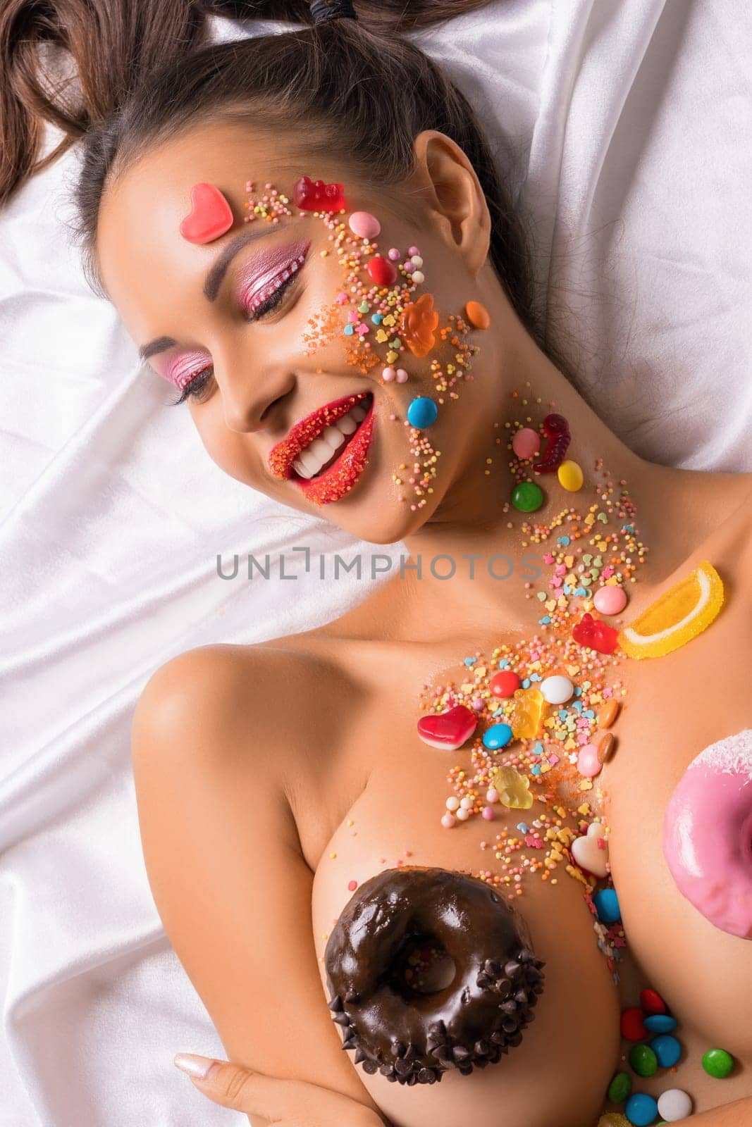 Brunette topless wearing red tanga with caramel makeup and bodyart and donuts on her breasts high angle shot