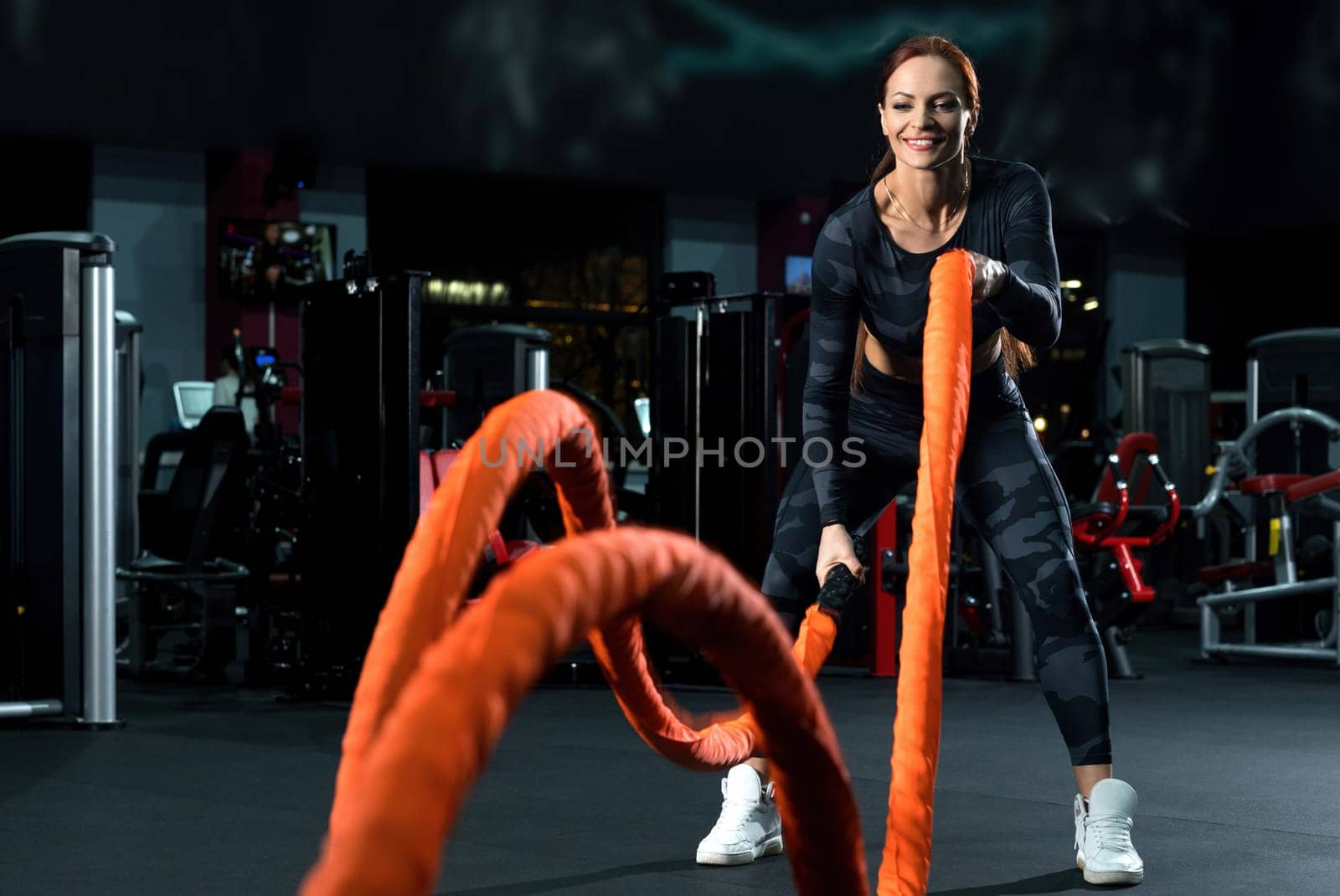 Slim brunette in sportswear doing exercises with a rope view in a gym