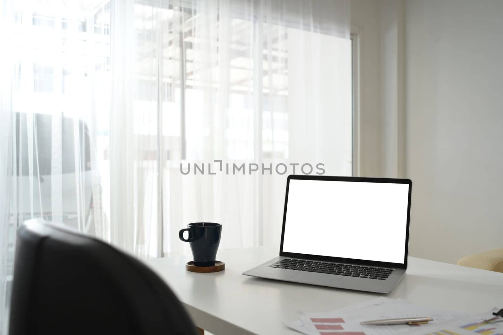 Laptop with blank screen, financial documents and cup of coffee on white table.