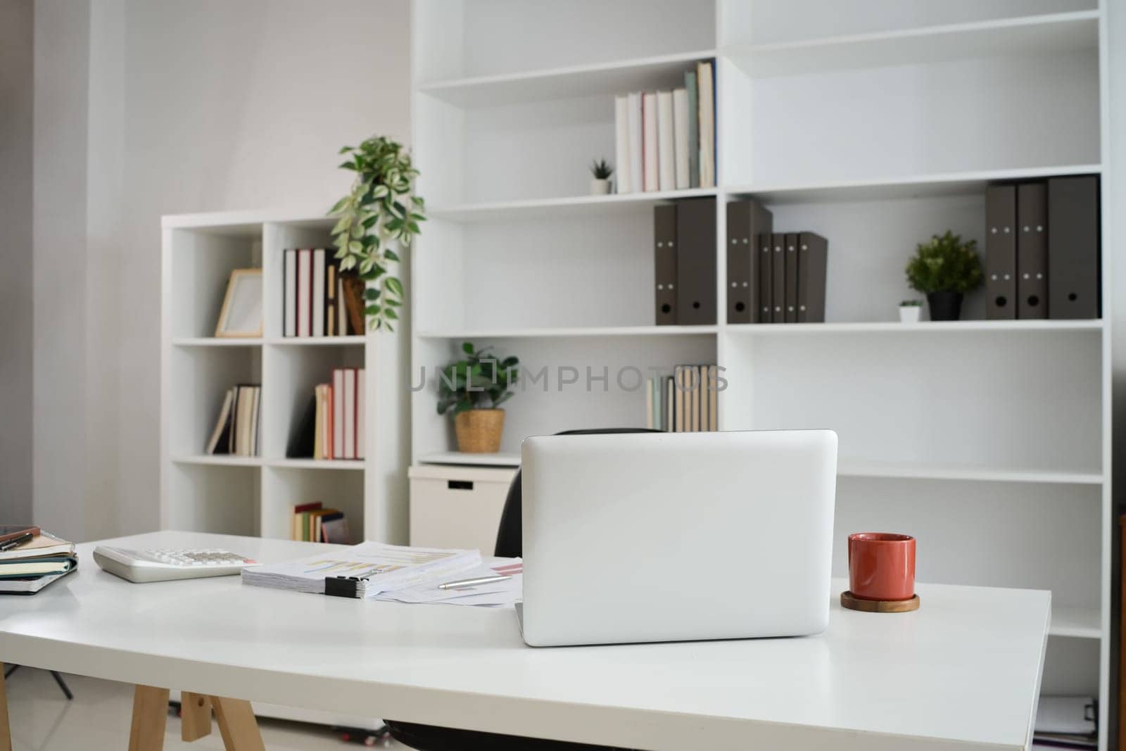 Laptop on white table with coffee cup, calculator and financial reports.