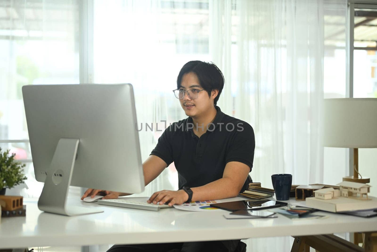 Handsome man working on project at desk surrounding with several architectural models and materials.