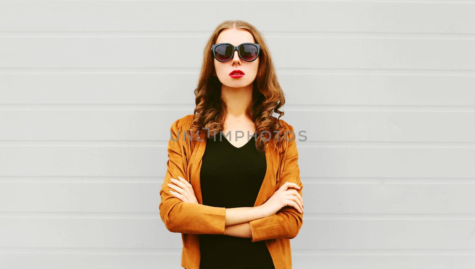 Fashion portrait pretty woman with crossed arms wearing a sunglasses, jacket over grey background