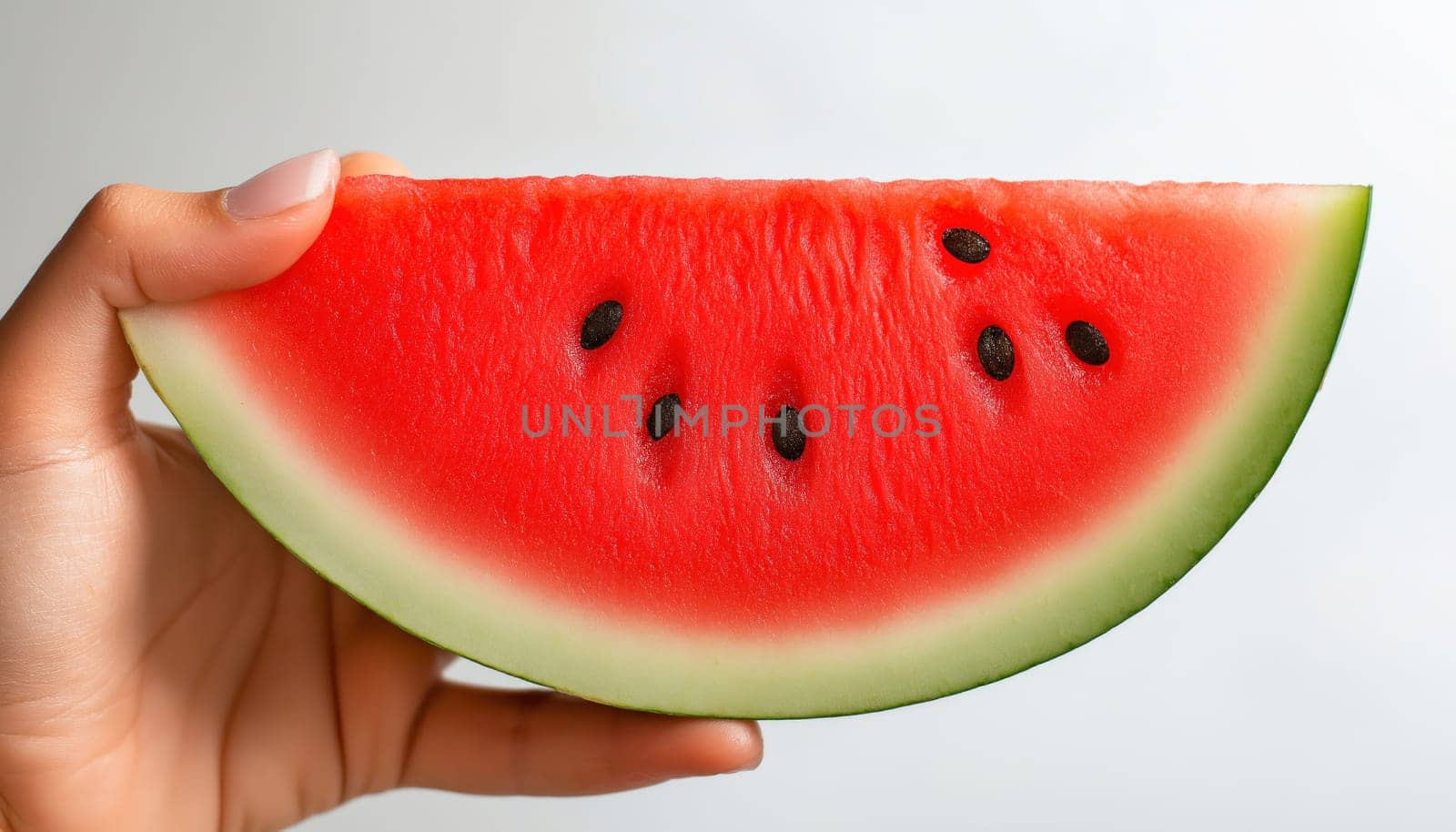 Hand holding a slice of ripe red watermelon with black seeds