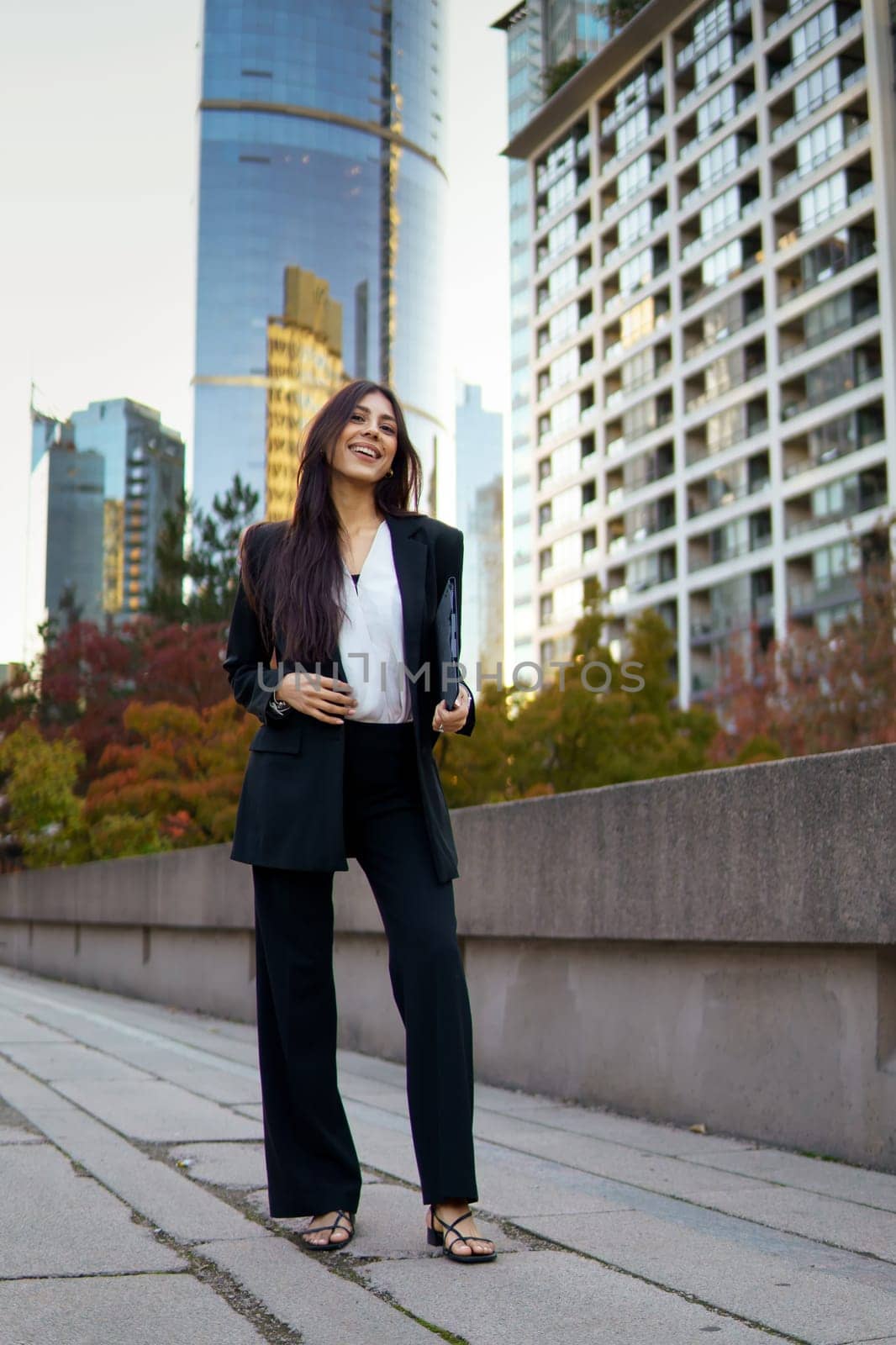 Portrait of hispanic businesswoman standing in an urban with tall glass buildings and autumn colored foliage.