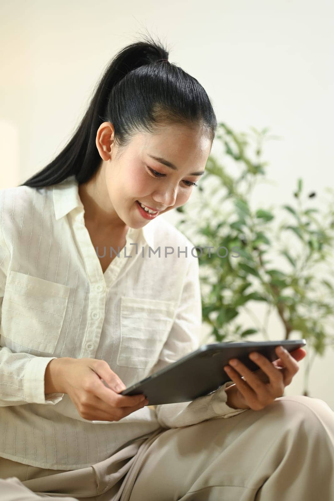 Attractive young woman browsing internet on digital tablet, sitting on sofa at home.