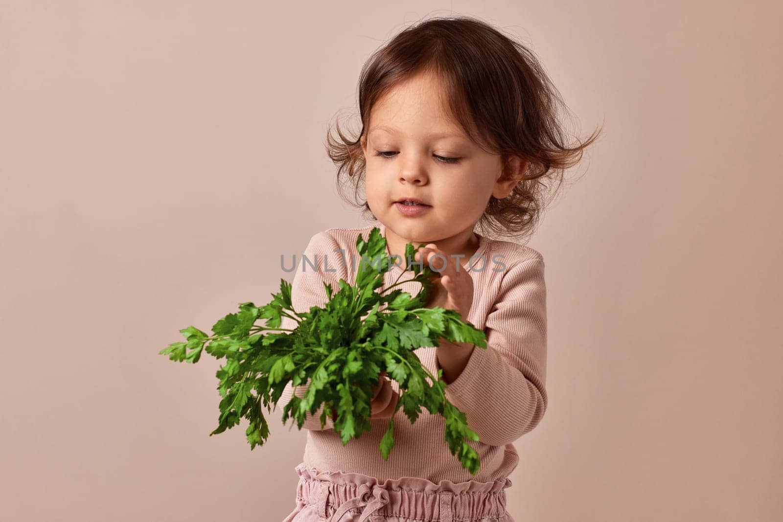 child girl holding fresh green parsley on beige background. healthy baby food.
