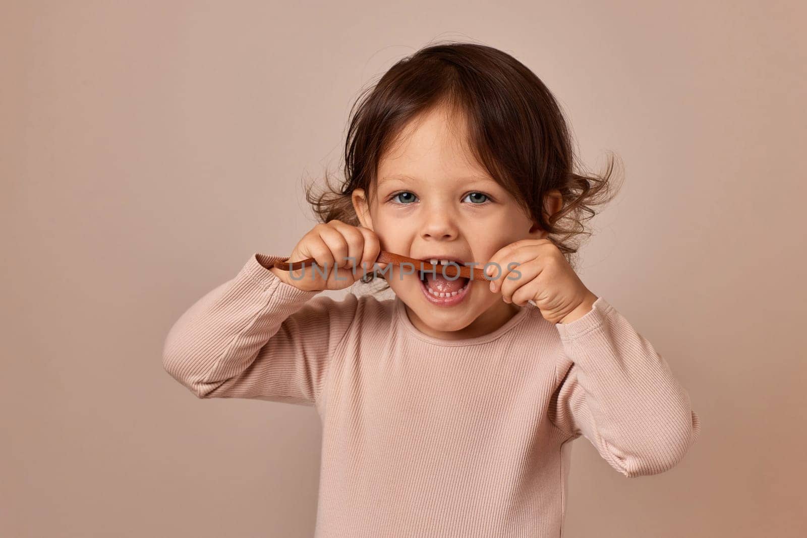 cute child girl bites fruit pastille on beige background. healthy baby food.
