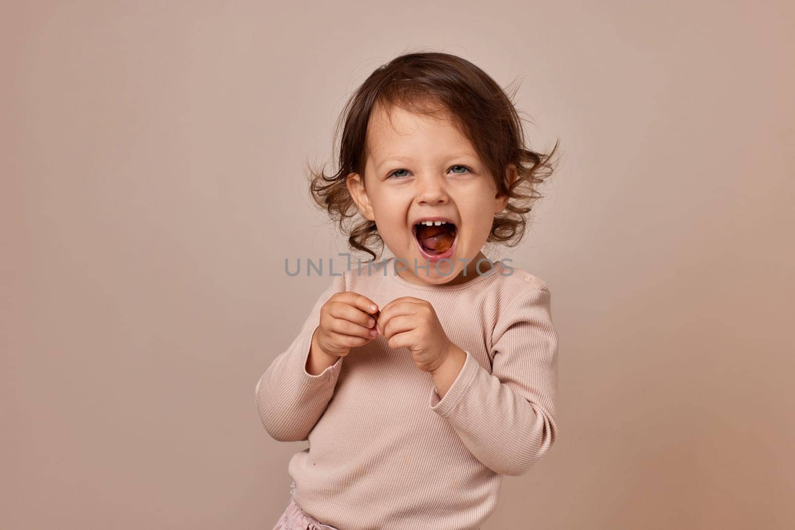 smiling very excited child girl holding fruit pastille on beige background. healthy baby food.