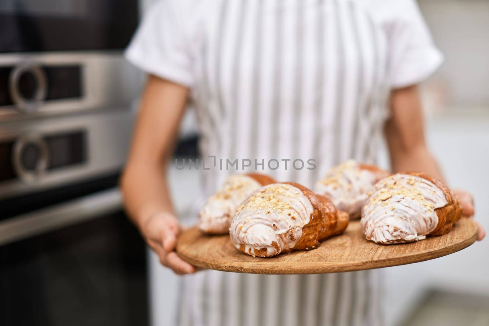female baker holding wooden tray with freshly baked crispy golden croissants