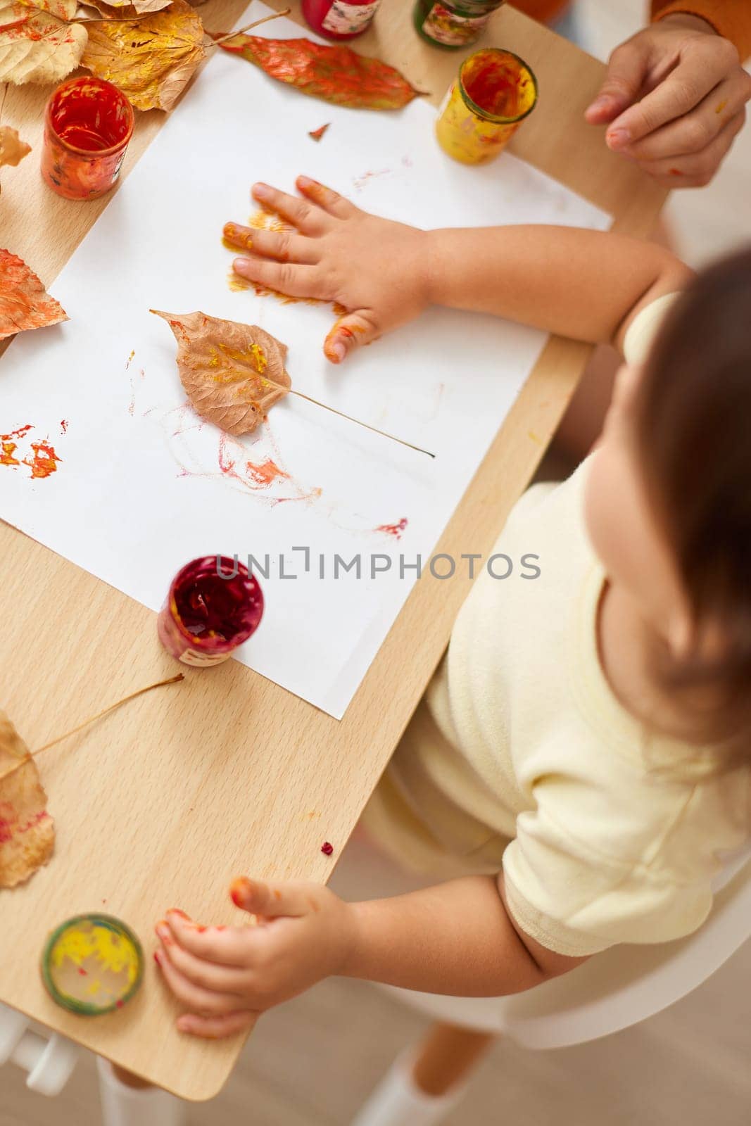 little child girl painting hands and autumn yellow leaves. kid leaves yellow handprints on paper, top view