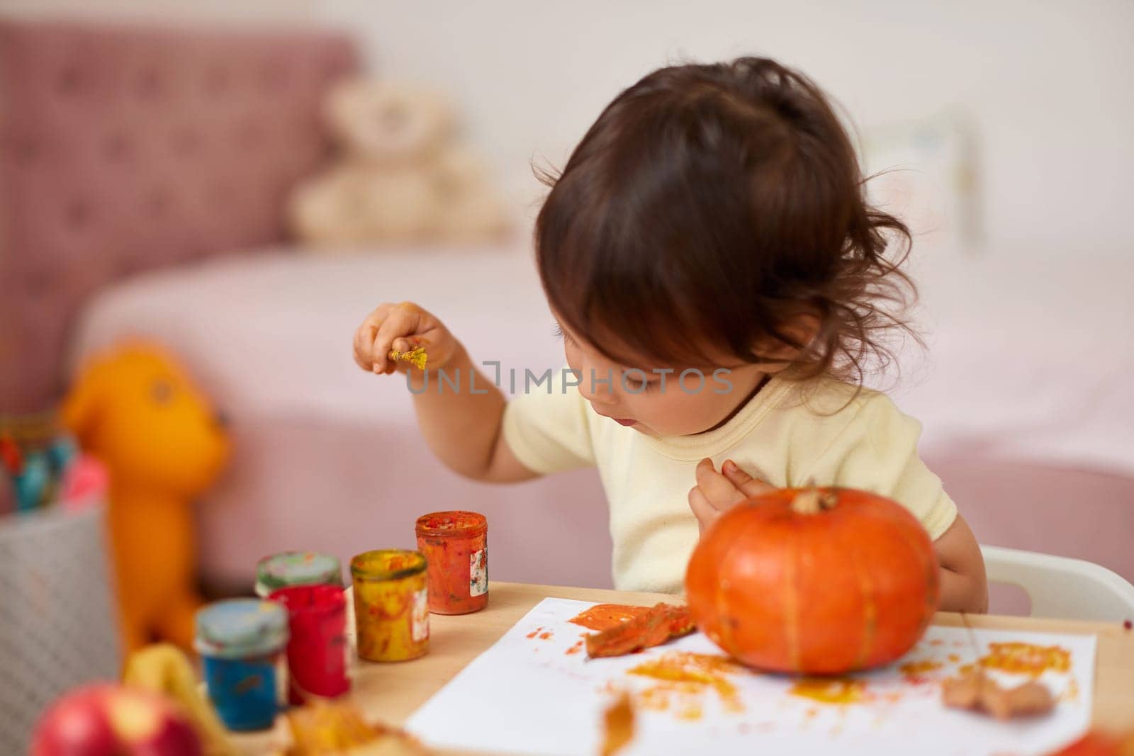 happy little child girl painting Halloween pumpkin. smiling baby girl drawing autumn pumpkin in yellow paint
